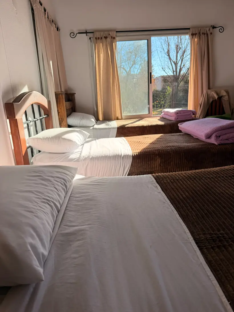 Habitación compartida con tres camas tendidas y toallas limpias junto al ventanal al jardín