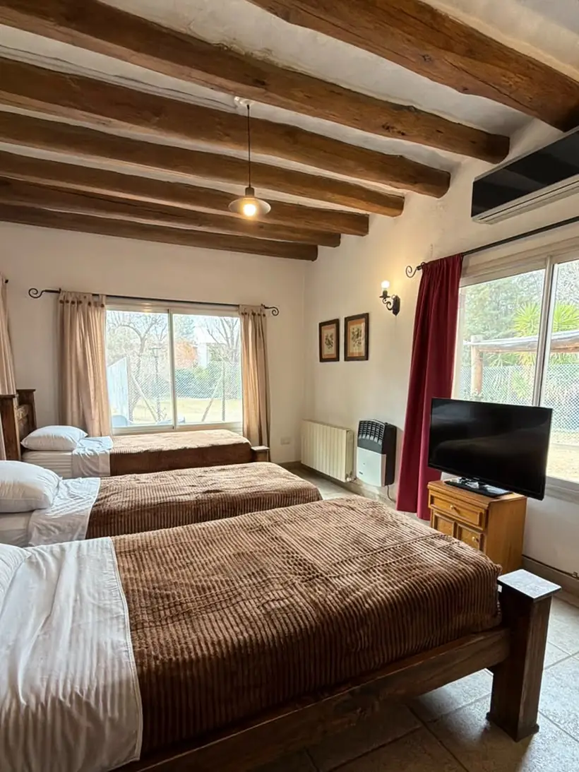 Habitación amplia bajo techo de vigas de madera, con tres camas y ventanas al jardín