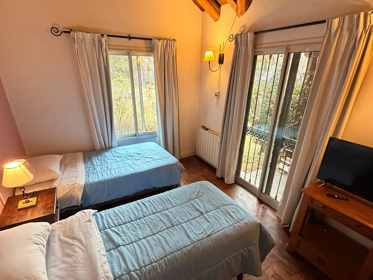 Habitación con dos camas, vigas de madera y ventanal al jardín