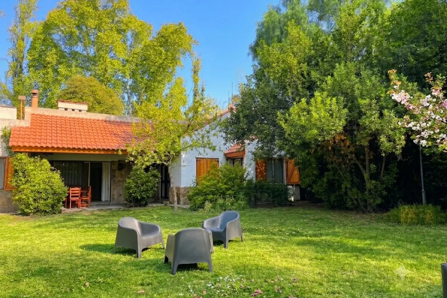 Casa de techo de tejas y parque con césped y sillones, en Chacras de Coria, Mendoza