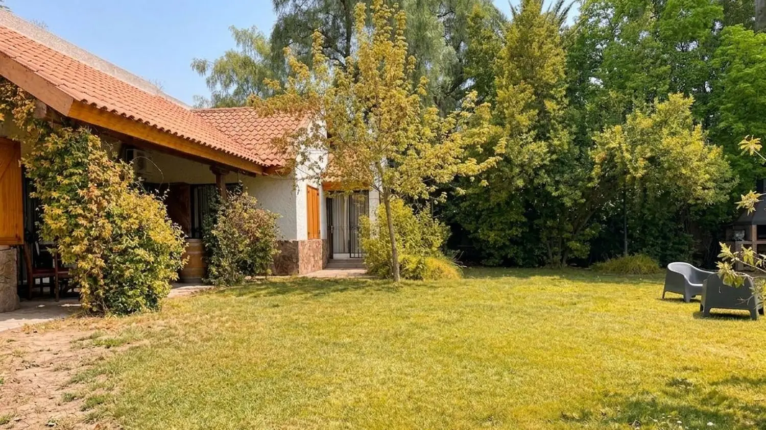 El parque arbolado de la casa, con la galería y el techo de tejas a un costado